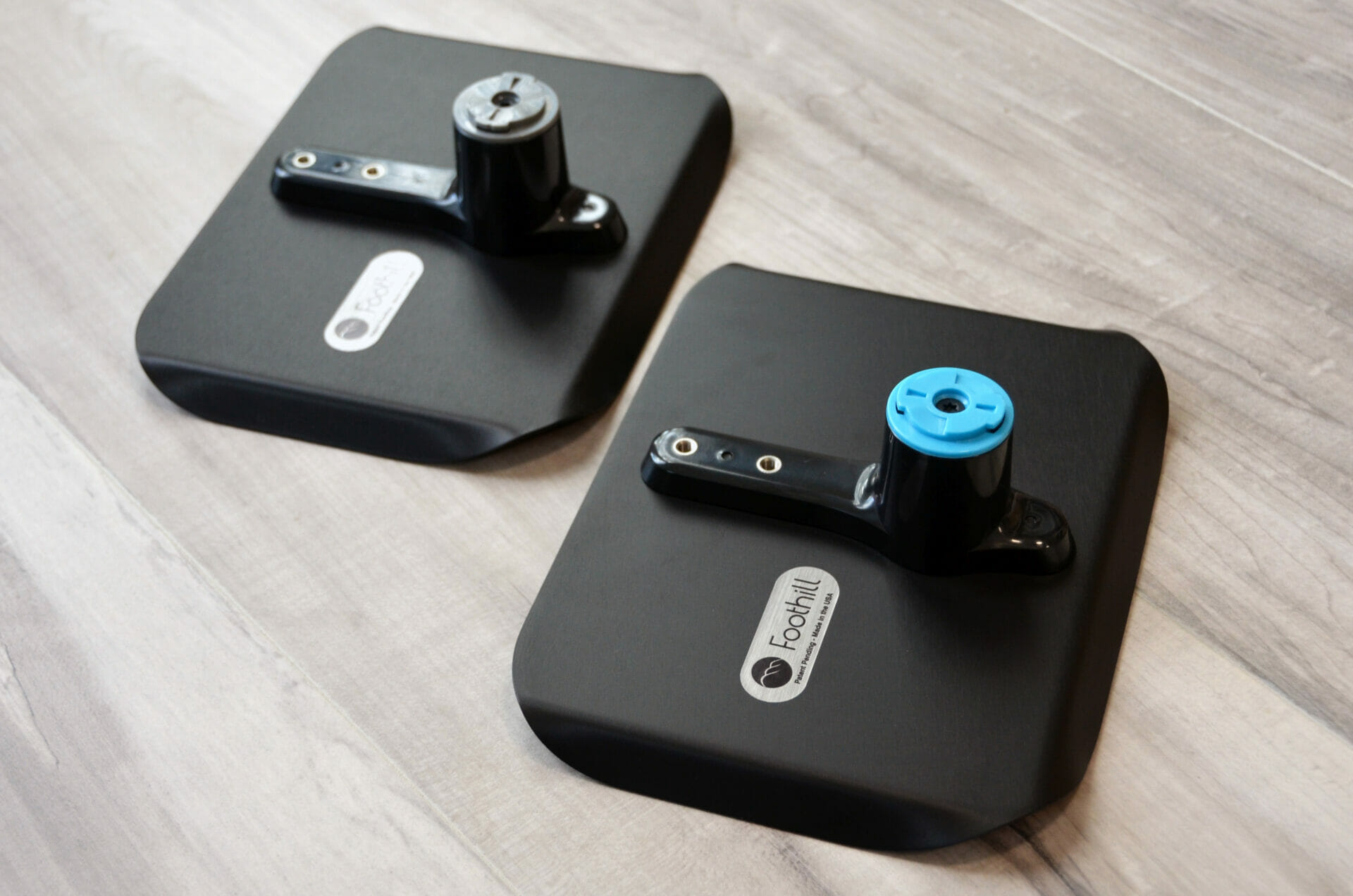 Two black anodized aluminum mount trays from Foothill products sitting face down on a wood floor, showing the Foothill logo etched into the bottom.
