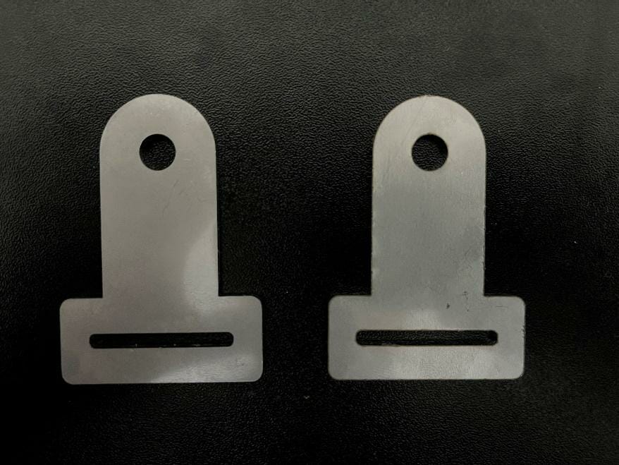 Image of two of the real brackets, laser cut out of aluminum and sitting on a steel table